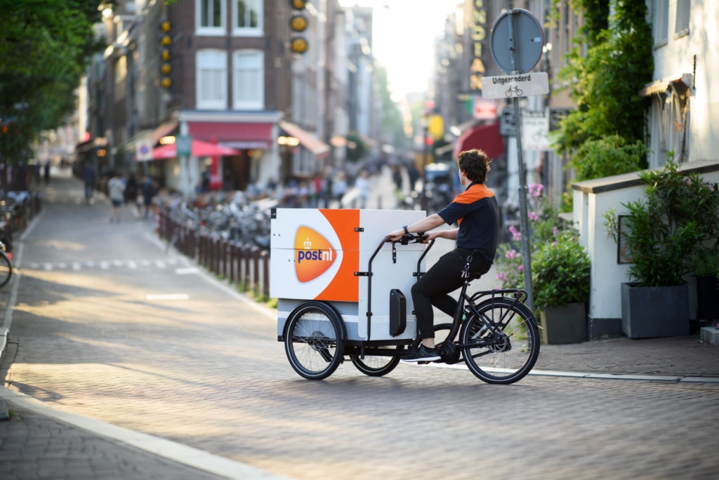 PostNL postbode op de bakfiets, rijdend door de straten van Amsterdam